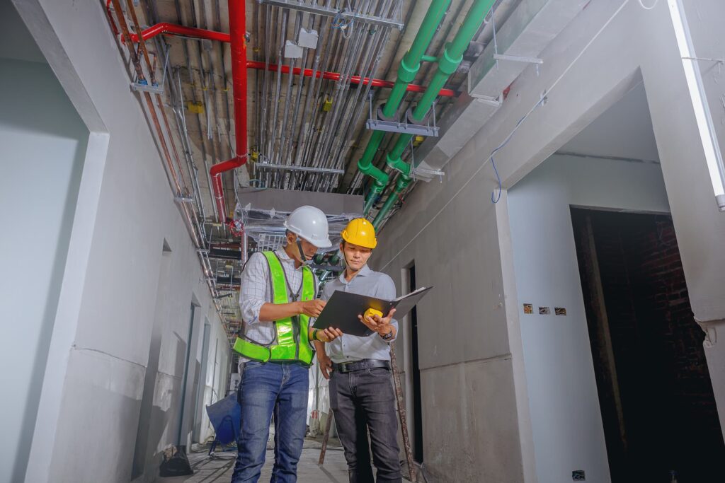 Engineers reviewing plans on a construction site with exposed ceiling utilities and piping